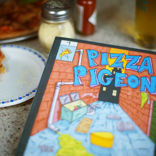 Pizza Pigeon, a graphic novel about a pigeon with pizza slices for wings, pictured here in front of a slice of pizza and a shaker of parmesan cheese.